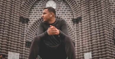 man in black long sleeve shirt and black pants sitting on brown brick wall