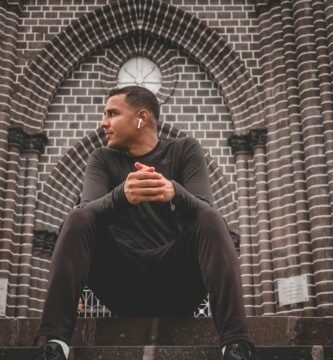 man in black long sleeve shirt and black pants sitting on brown brick wall